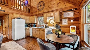 Interior de una cabaña de madera con cocina, comedor y un reloj en la pared.