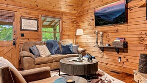 Interior de una cabaña de madera con sofá, mesa de centro y televisor montado.