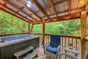 Eine Holzterrasse mit Whirlpool, Korbstühlen und einem Tisch mit einer Laterne.