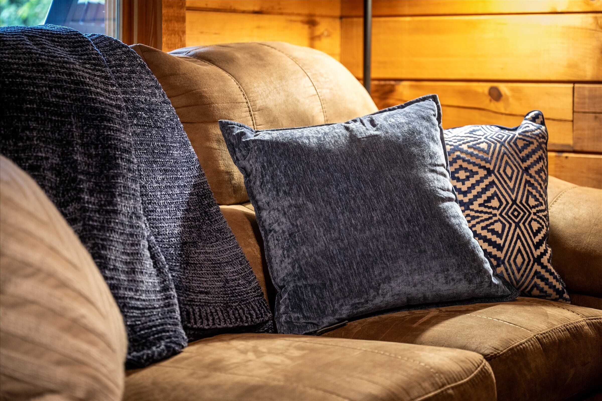 A brown leather sofa with three pillows, one with a geometric pattern.