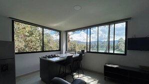 A modern kitchen with a central island, bar stools, and large windows offering a view of trees and mountains. - Charming 1-bedroom apartment in soothing Guatapé perfect for getaway (Guatapé)