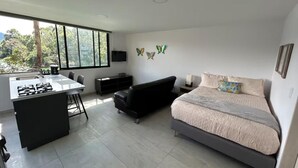 A modern bedroom with a bed, a sofa, a kitchen area with a stove, and large windows. - Charming 1-bedroom apartment in soothing Guatapé perfect for getaway (Guatapé)