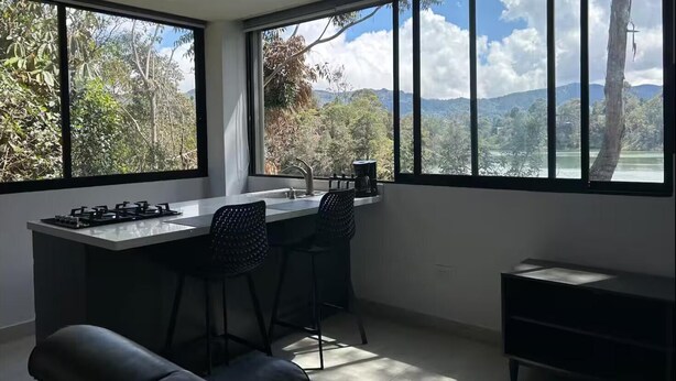 A modern kitchen with a large window, a gas stove, two bar stools, and a view of a mountainous landscape. - Charming 1-bedroom apartment in soothing Guatapé perfect for getaway (Guatapé)