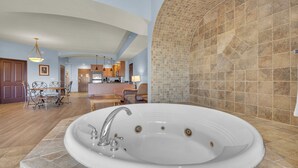 Une salle de bain spacieuse avec une grande baignoire, un espace douche séparé et une cuisine en arrière-plan.