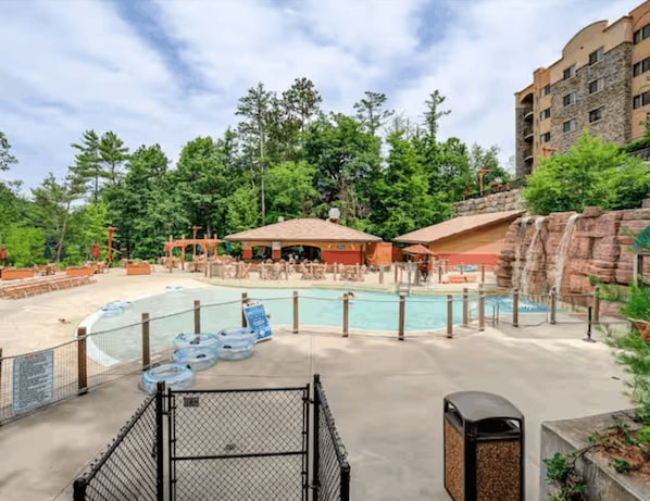 A pool area with a water slide, lounge chairs, and a building with a stone facade.