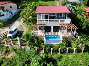 A two-story house with a red roof, a swimming pool, and a fenced patio area. - Infinity Pool & Ocean View Studio - Sunrise (Santos Guardiola)
