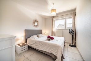 Une chambre à coucher avec un lit, une table de chevet, une lampe et un ventilateur sur pied.