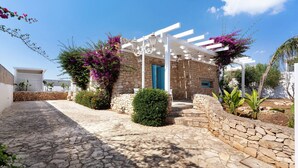Un edificio de piedra con una pérgola blanca, un muro de piedra y un camino adoquinado.