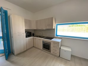 Una cocina compacta con armarios de madera clara, horno empotrado, un lavamanos y un refrigerador pequeño.