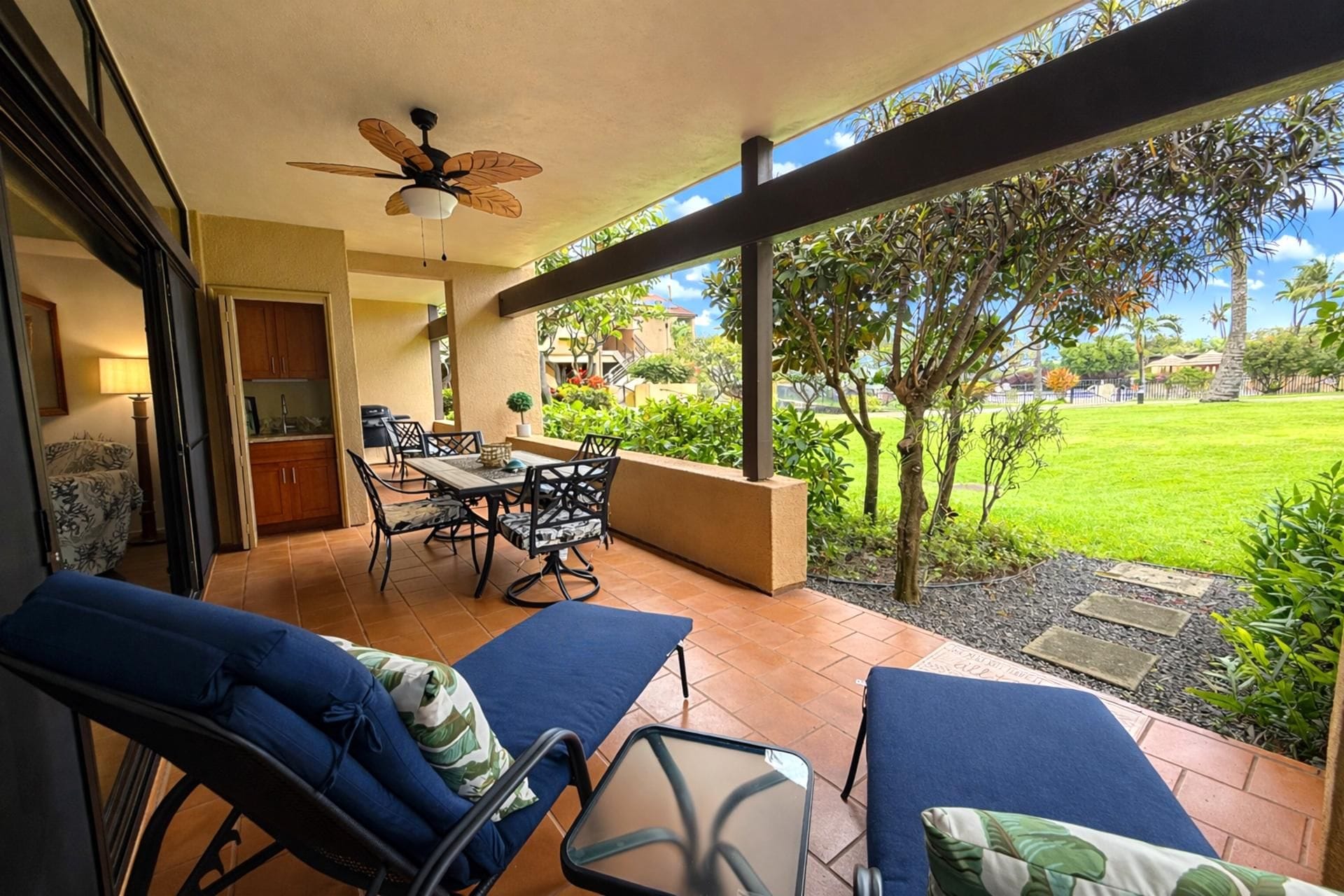 Un patio con una mesa y sillas de comedor, un ventilador de techo y vista a un área verde.