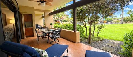 Un patio con una mesa y sillas de comedor, un ventilador de techo y vista a un área verde.
