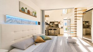 A bedroom with a bed, pillows, a bedside table, a headboard, a wall-mounted shelf with plants, and a view into the kitchen. - Apartment 'Venti Nodi' with Balcony, Wi-Fi and Air Conditioning (Vieste)