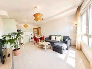 A modern apartment with a dining area, a grey sofa, and a kitchen in the background. - Dragos Suites 208 (Arrecife)