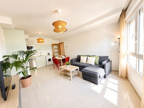 Eine moderne Wohnung mit Essbereich, einem grauen Sofa und einer Küche im Hintergrund.