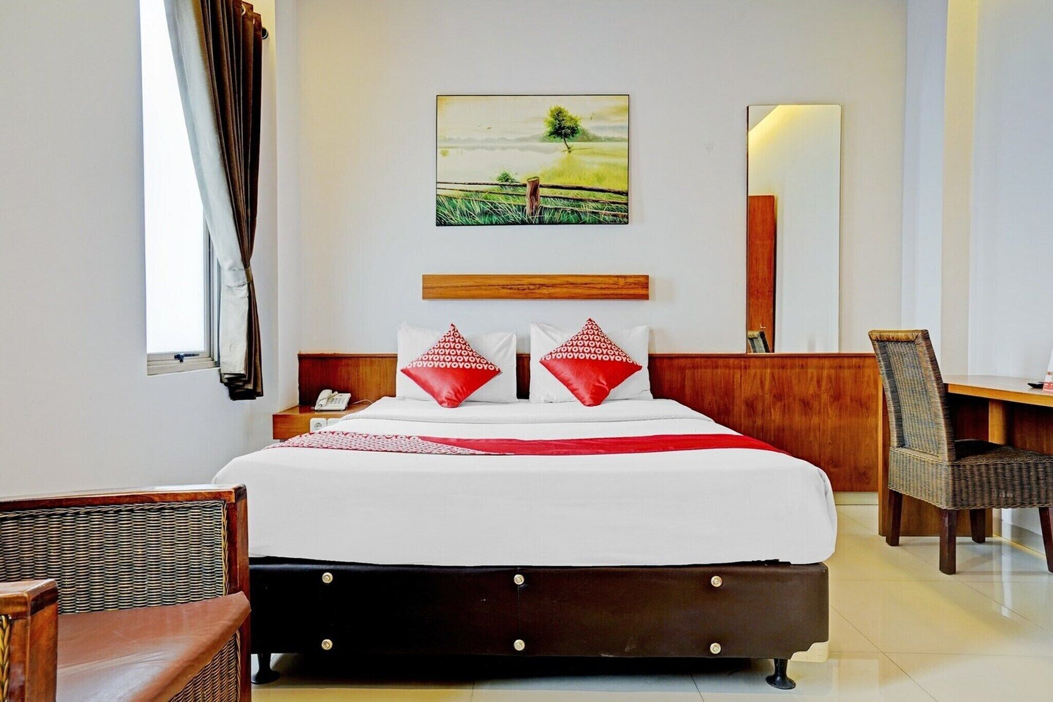 Ein Hotelzimmer mit Bett, Stuhl, Schreibtisch, einem Gemälde und einem Spiegel.