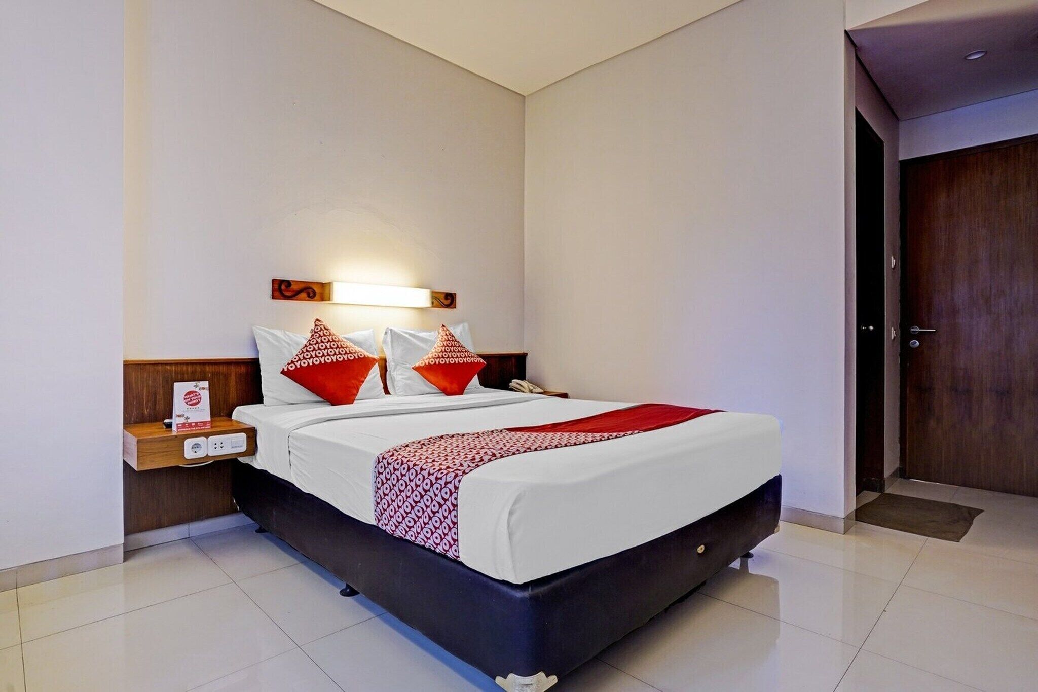 A modern hotel room with a large bed, a bedside table with a phone, and a wall-mounted light fixture.
