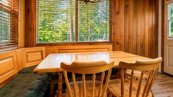 Un interior de madera con una mesa de comedor, sillas, un banco y un ventanal con persianas.