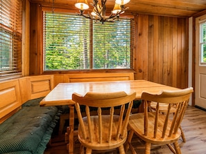 A wooden interior with a dining table and chairs, a bench, and a large window with blinds. - Teacher's Dream (Big Bear Lake)