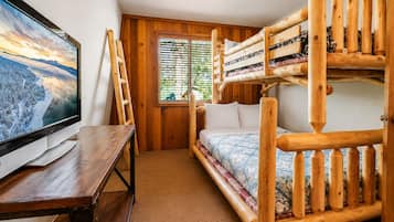 Habitación con literas, un televisor sobre una mesa de madera, una ventana con persianas y piso alfombrado.