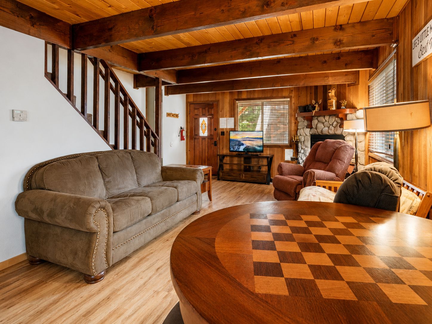 Una sala de estar acogedora con una escalera de madera, un sofá de cuero, una mesa de centro de madera y un suelo a cuadros.