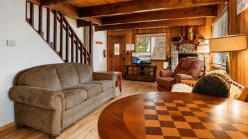 Una sala de estar acogedora con una escalera de madera, un sofá de cuero, una mesa de centro de madera y un suelo a cuadros.