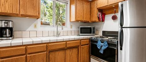 A kitchen with wooden cabinets, a stainless steel refrigerator, a microwave, and a stove.