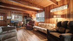 L’intérieur chaleureux d’un chalet avec des murs en bois, une cheminée, un canapé et un téléviseur.