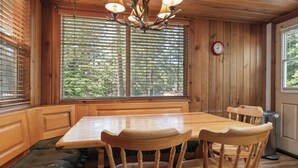 Un coin repas en bois avec une table et des chaises, un banc, une fenêtre avec des stores et une horloge au mur.