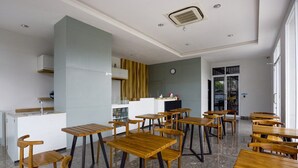 A modern dining area with wooden tables and chairs, a kitchen in the background, and a clock on the wall. - Luxury Deluxe DBL Escape W/ Free WiFi and Parking (Bekasi)