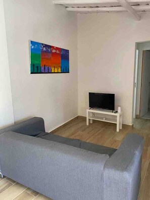 A living room with a grey sofa, a flat-screen TV on a white stand, and a colorful abstract painting on the wall.