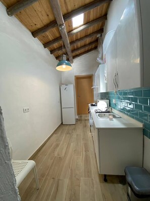 A narrow kitchen with a wooden ceiling, a white refrigerator, a sink, and a tiled backsplash.
