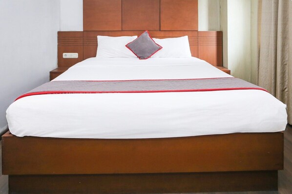 Una cama bien hecha con cabecera de madera, ropa de cama blanca y un toque de rojo.