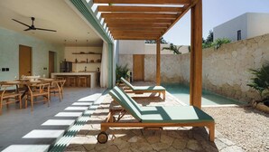 Une terrasse extérieure moderne, dotée de chaises longues en bois, d’un espace repas et d’une cuisine.