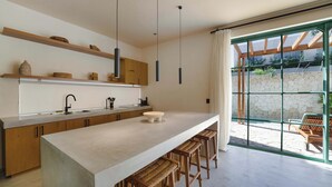 Une cuisine moderne dotée d’un îlot central, de tabourets de bar, de luminaires suspendus et offrant une vue sur la terrasse extérieure.