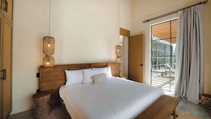 Une chambre avec un grand lit, une tête de lit en bois, des lampes en osier, un banc et une vue sur l’extérieur, visible à travers une porte vitrée.