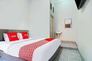 Ein Hotelzimmer mit einem Bett, einem Nachttisch, einem an der Wand befestigten Fernseher und einem kleinen Fenster.