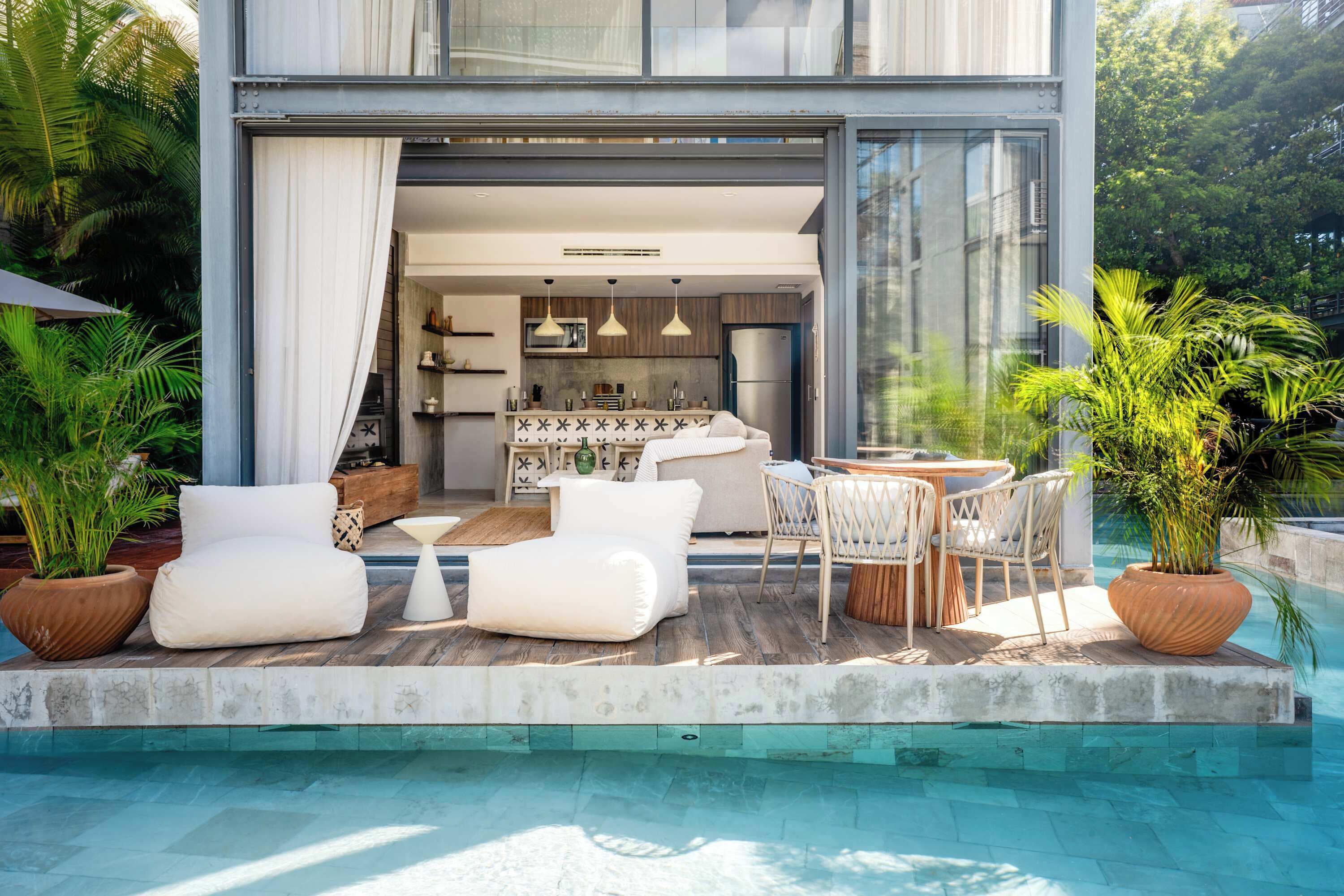 A modern house with a pool, outdoor seating, and a kitchen visible through an open door.