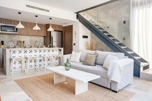 A modern kitchen with pendant lights, a built-in microwave, and a central island with stools. - Modern 1BR at Xalet Luxury Condos | Cenote & Pool (Tulum)