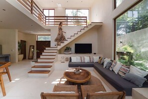 Un vaste espace de vie comprenant un escalier, un grand canapé, une table basse et un téléviseur.