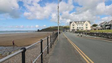 A coastal road with a beach on one side, a stone wall, and a row of buildings with a traditional architectural style.