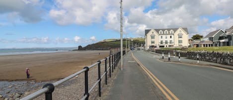 A coastal road with a beach on one side, a stone wall, and a row of buildings with a traditional architectural style.