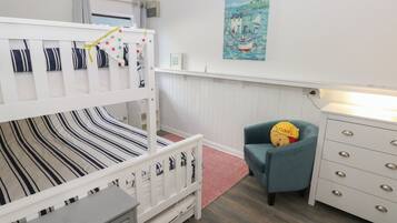 A bunk bed with striped bedding, a chair with a cushion, a dresser with drawers, a painting on the wall, and a red rug.