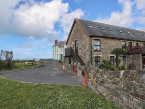 A stone building with a paved driveway, a wooden fence, and a grassy area with white flowers. - Puffin Nook, 2 The Coach House, Broad Haven (Haverfordwest)