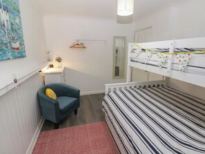 A bunk bed with star-patterned bedding, a blue armchair, a small desk with a lamp, and a wall with a maritime-themed painting. - Puffin Nook, 2 The Coach House, Broad Haven (Haverfordwest)
