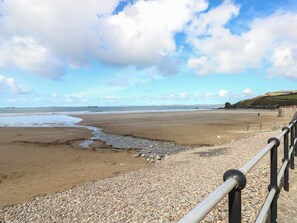 A beach with a pebble foreground, a metal railing, and a distant view of the sea and hills. - Puffin Nook, 2 The Coach House, Broad Haven (Haverfordwest)