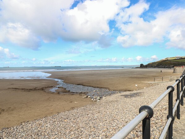 A beach with a pebble foreground, a metal railing, and a distant view of the sea and hills. - Puffin Nook, 2 The Coach House, Broad Haven (Haverfordwest)