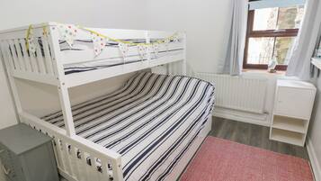 Una cama individual con ropa de cama a rayas, un radiador, una ventana con cortinas y un mueble pequeño.