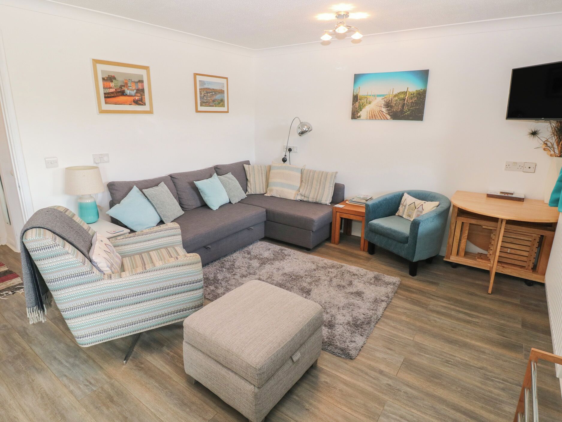 A living room with a sectional sofa, a blue armchair, a small table, and a TV.