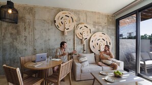 Een modern interieur met een ronde houten tafel, rieten stoelen, een bank en een bijzettafeltje met een fruitschaal.