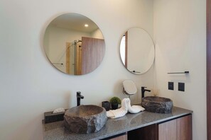 A bathroom with a granite countertop, two stone sinks, a mirror, and a towel rack. - Modern 2BR Apartment with Pool & Gym (Tulum)